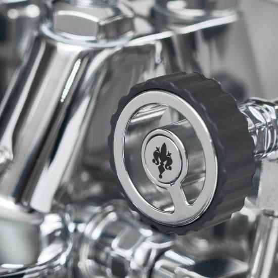 Close-up van een glanzende chromen draaiknop op een espressomachine bij Espresso Werkplaats